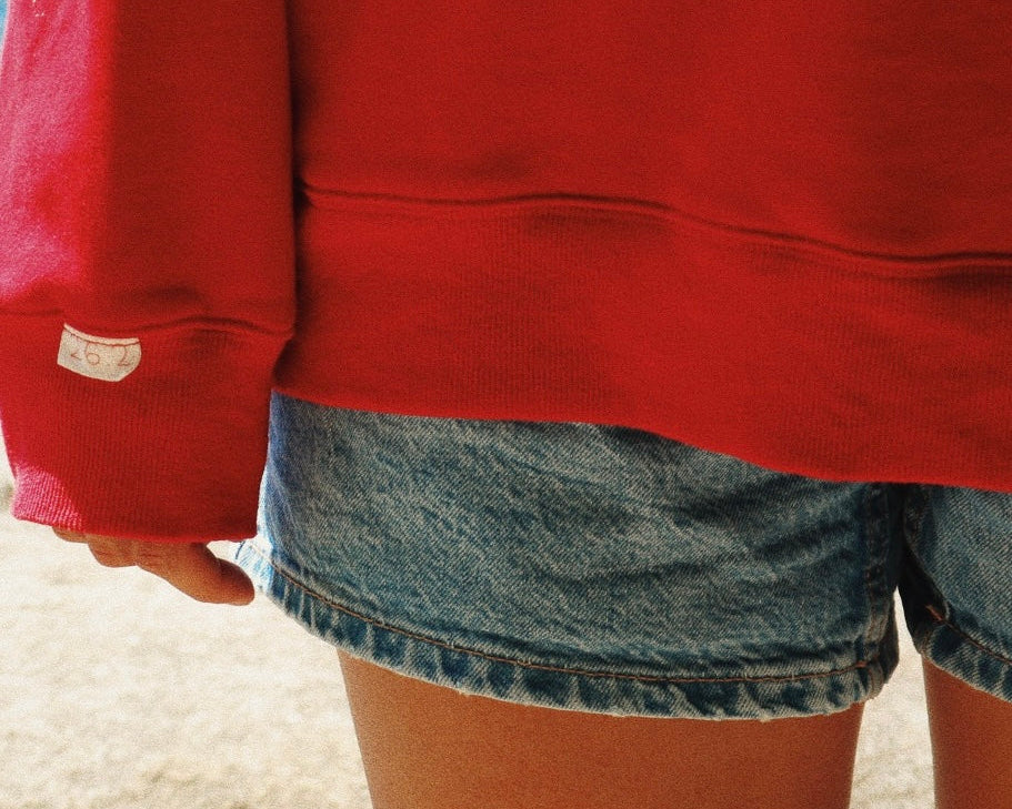 Person wearing a red sweatshirt and denim shorts on a beach.