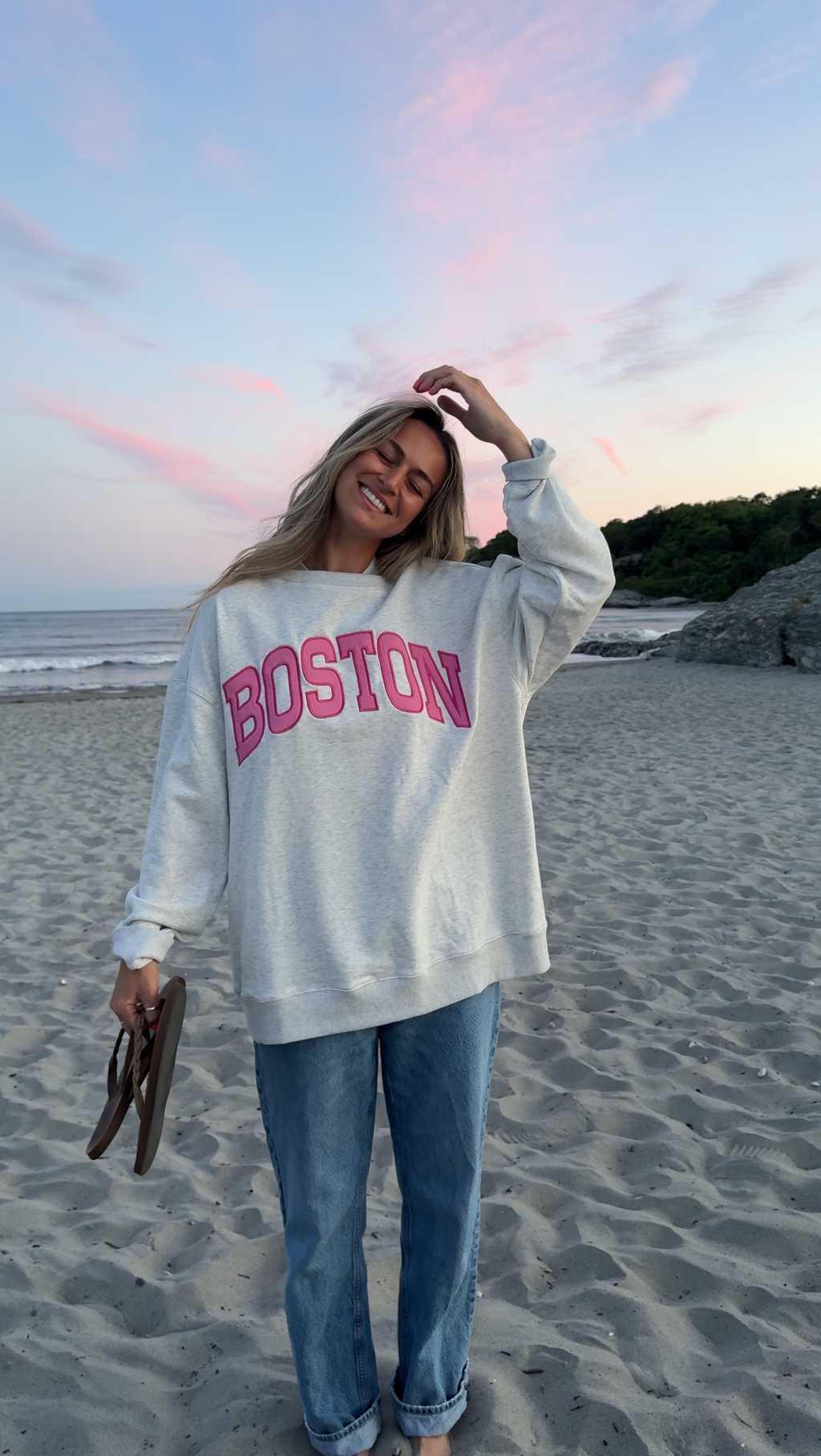 Person wearing a 'Boston' berry breeze sweatshirt on a beach at sunset