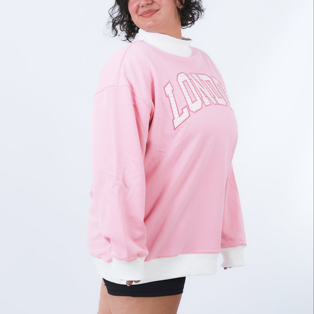 Person wearing a pink sweatshirt with 'LONDON' printed on it against a white background
