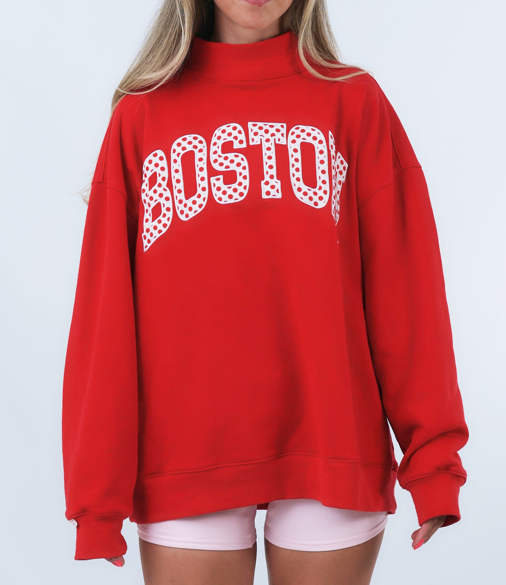 Person wearing a red sweatshirt with 'BOSTON' printed on it against a white background