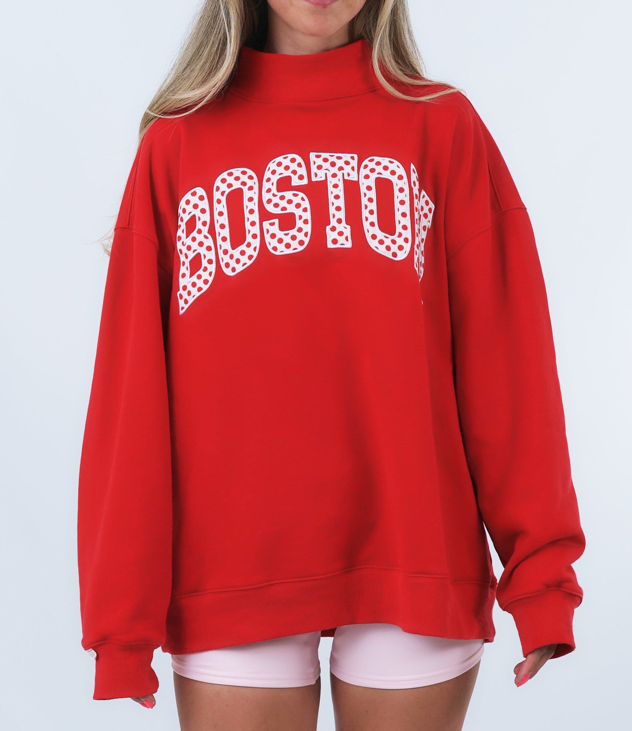 Person wearing a red sweatshirt with 'BOSTON' printed on it against a white background